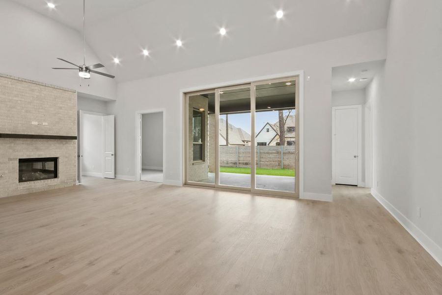 Unfurnished living room with high vaulted ceiling, baseboards, a fireplace, a ceiling fan, and light wood-style floors Unfurnished living room with high vaulted ceiling, baseboards, a fireplace, a ceiling fan, and light wood-style floors