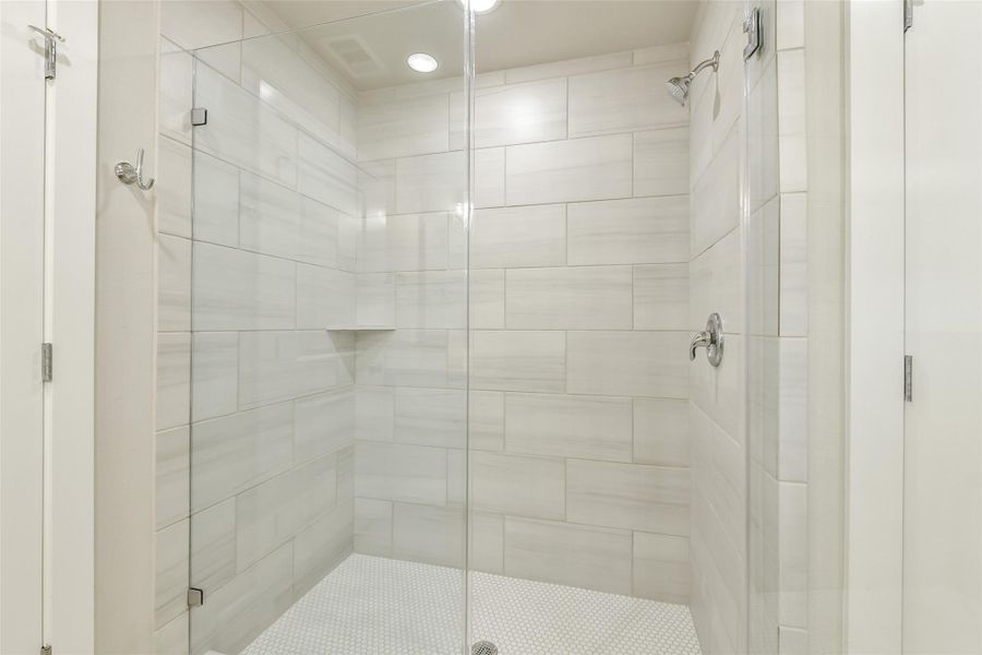 Spacious walk-in shower with floor-to-ceiling tile, built-in niche and sleek frameless glass enclosure.