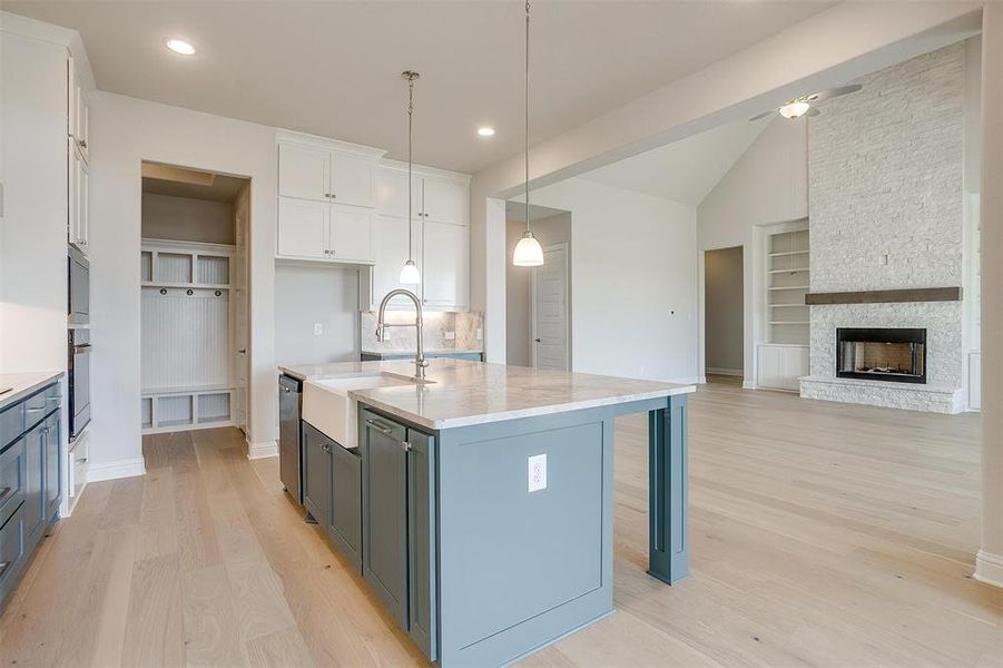 Kitchen with white cabinets, hanging light fixtures, an island with sink, a fireplace, and sink