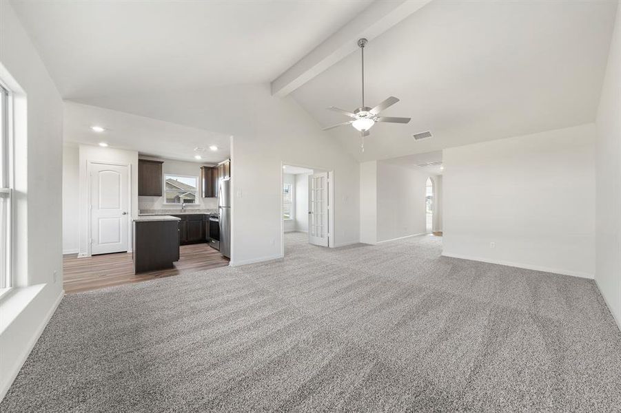 Unfurnished living room featuring ceiling fan, beamed ceiling, light colored carpet, high vaulted ceiling, and sink