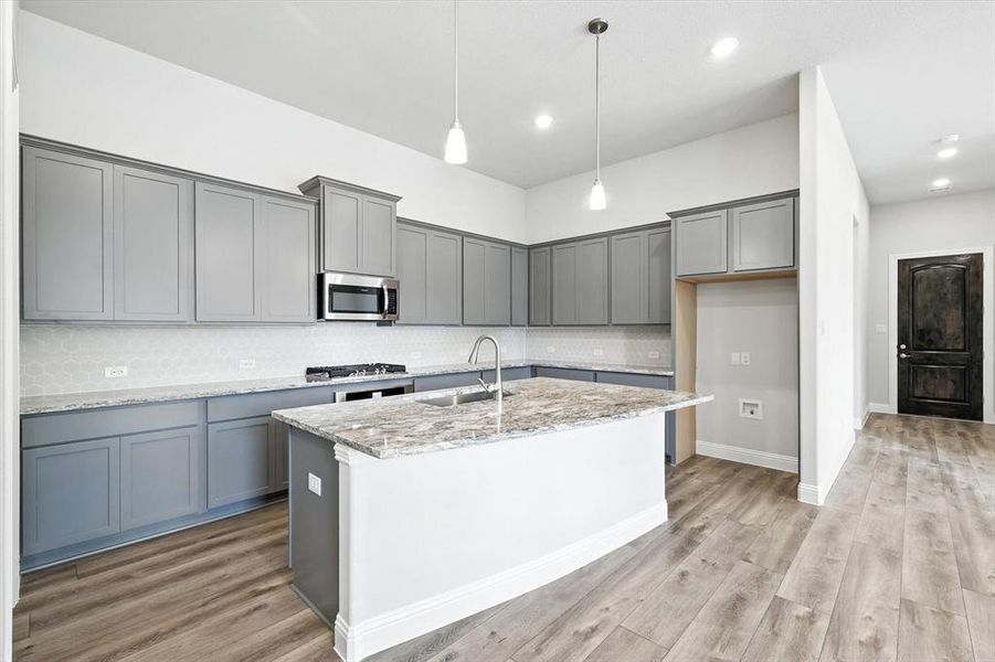 Kitchen with gray cabinetry, a kitchen island with sink, light stone countertops, hanging light fixtures, and recessed lighting Kitchen with gray cabinetry, a kitchen island with sink, light stone countertops, hanging light fixtures, and recessed lighting