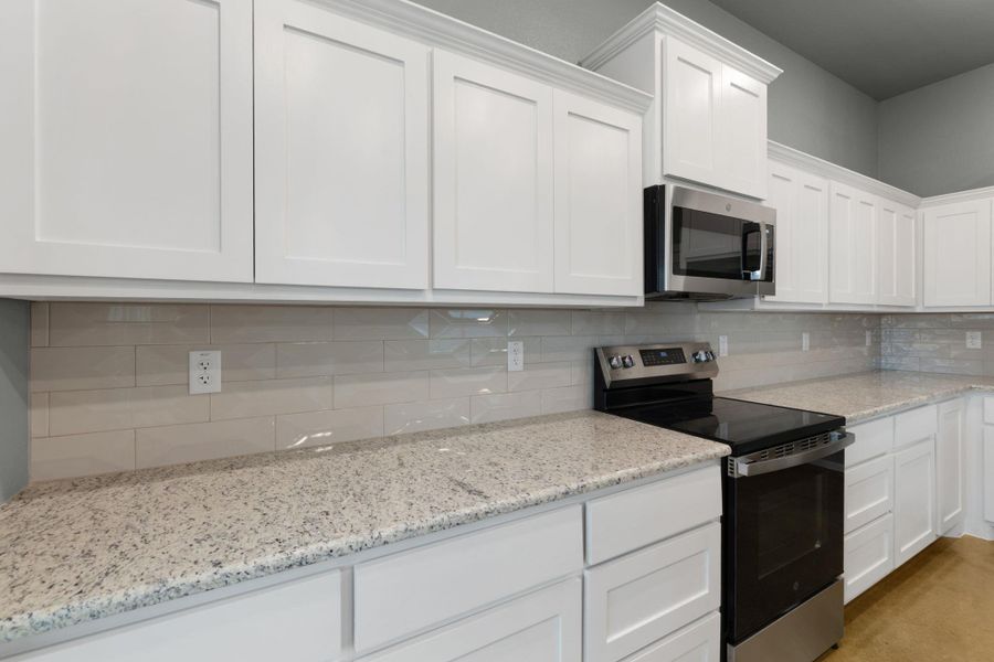 Culinary delights await in this bright kitchen with ample white cabinetry and gleaming stone counters.