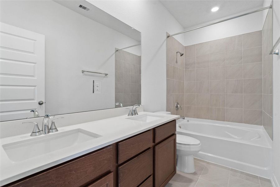 This move-in ready primary bathroom offers a spacious tub/shower combination with a tiled surround, stained cabinetry topped with light countertops, dual sinks, high ceilings, neutral paint, a large mirror, and sleek, modern finishes for a polished look.