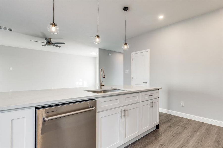 Kitchen featuring stainless steel dishwasher, sink, hanging light fixtures, and white cabinets