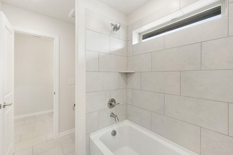 Bathroom with tub-shower combo, large light gray tile surround, and small window above
