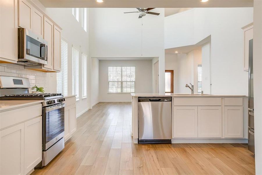 Kitchen with light hardwood / wood-style floors, a towering ceiling, white cabinetry, and appliances with stainless steel finishes