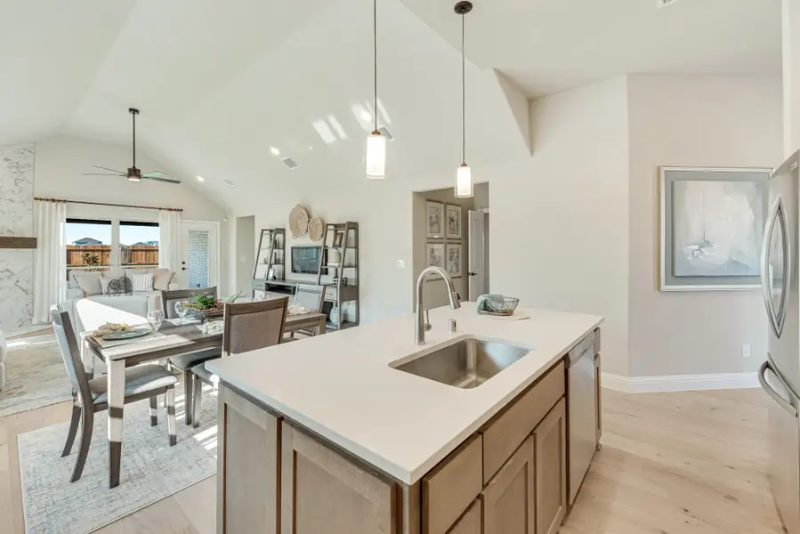 Kitchen island with sink and pendant lights, open to dining area and living room with vaulted ceiling