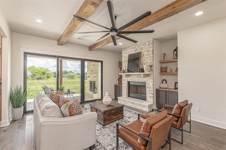Living room featuring a ceiling fan, hardwood / wood-style flooring, a stone fireplace, beam ceiling, and recessed lighting