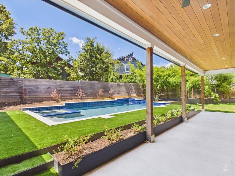 An inviting covered patio looks out onto a sparkling pool and manicured lawn.