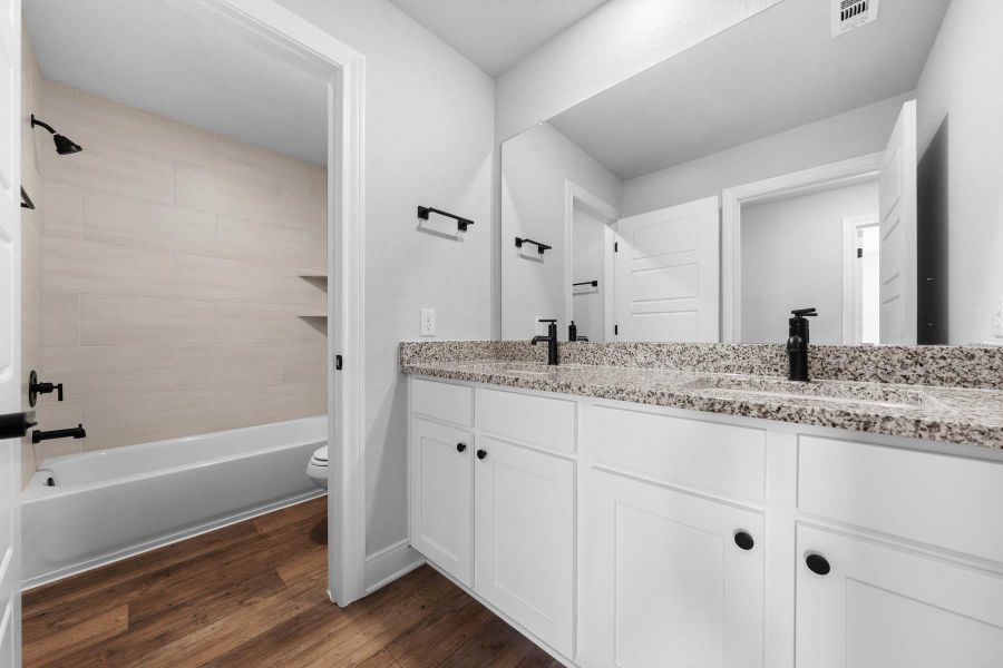 Bathroom with double vanity, dark wood-style flooring, and shower / bathtub combination