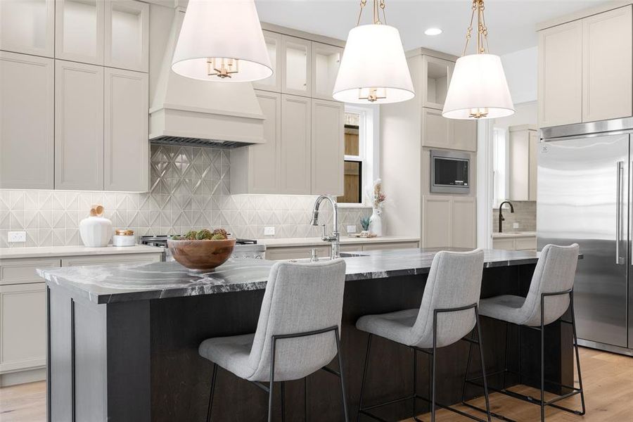 Kitchen with light wood-style flooring, built in appliances, backsplash, glass insert cabinets, and hanging light fixtures Kitchen with light wood-style flooring, built in appliances, backsplash, glass insert cabinets, and hanging light fixtures