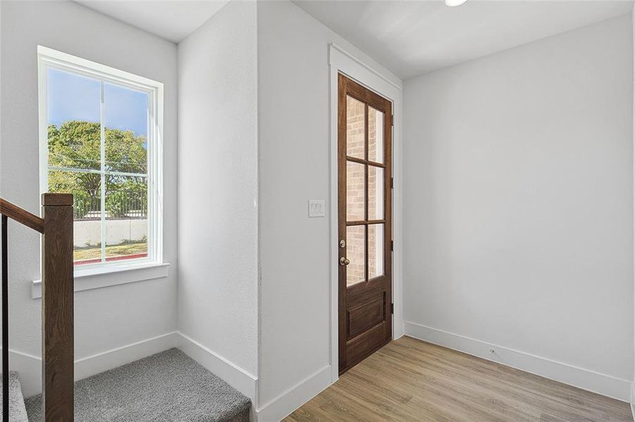 The entryway features a dark wood paneled door with glass inserts, complemented by light wood flooring