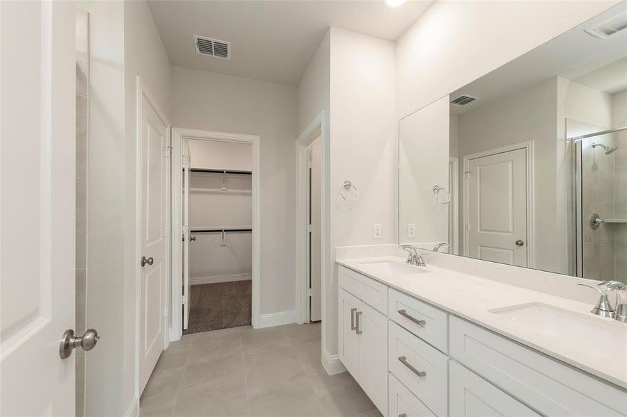 Bathroom with a stall shower, a spacious closet, tile patterned floors, double vanity, and baseboards Bathroom with a stall shower, a spacious closet, tile patterned floors, double vanity, and baseboards