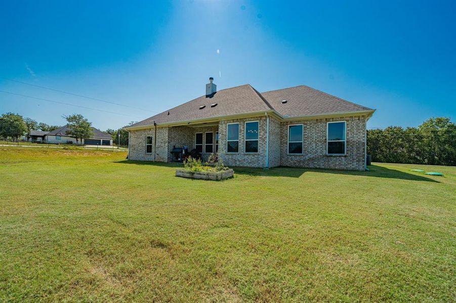 Back of property with a yard, brick siding, a patio area, and a shingled roof Back of property with a yard, brick siding, a patio area, and a shingled roof