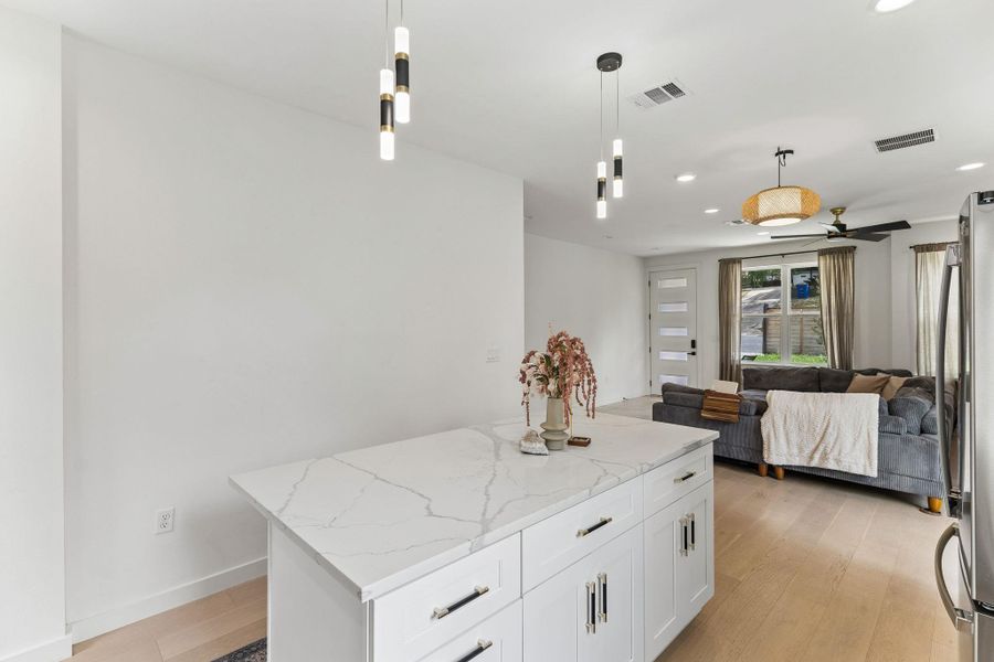 A clean, minimalist view of the kitchen island against a crisp white wall, looking toward the entryway. This shot highlights the modern lighting fixtures and the consistent, high-quality finishes found throughout the home.