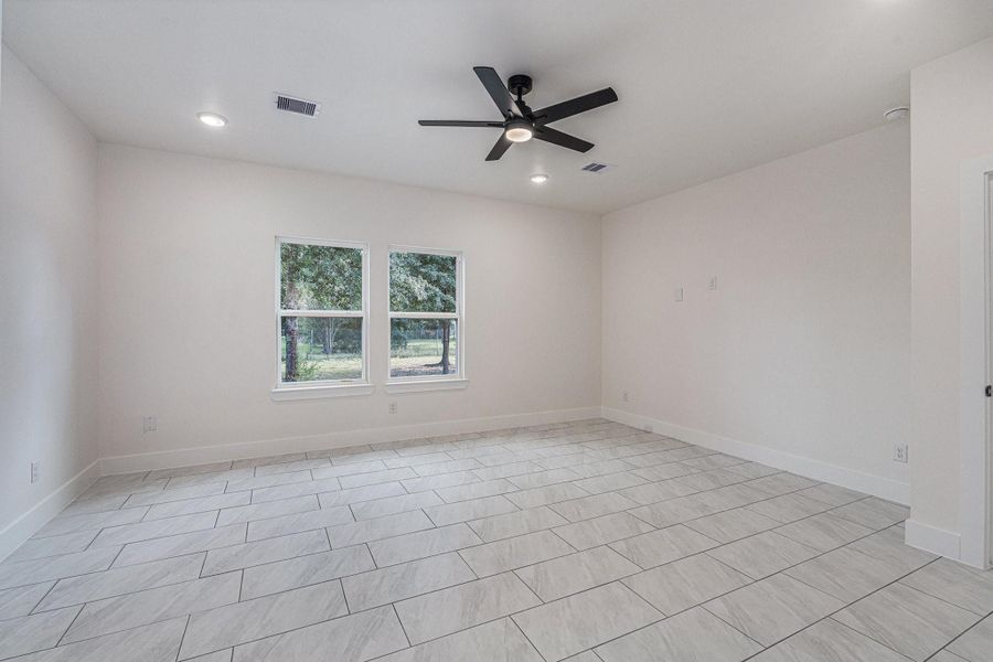 This spacious room features light tile flooring, neutral walls, and two large windows for natural light. It includes recessed lighting and a modern ceiling fan, creating a bright and airy atmosphere.