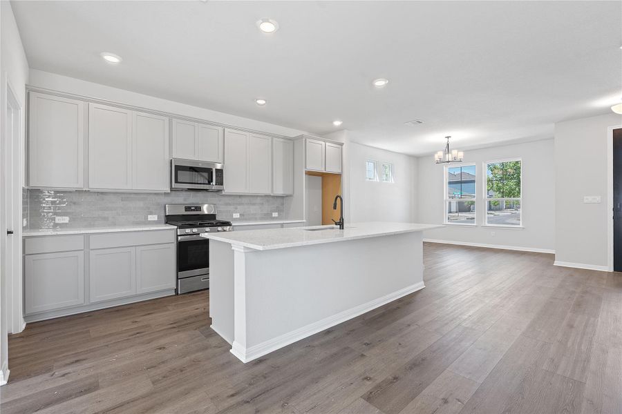 Kitchen featuring appliances with stainless steel finishes, a chandelier, tasteful backsplash, light wood finished floors, and a kitchen island with sink