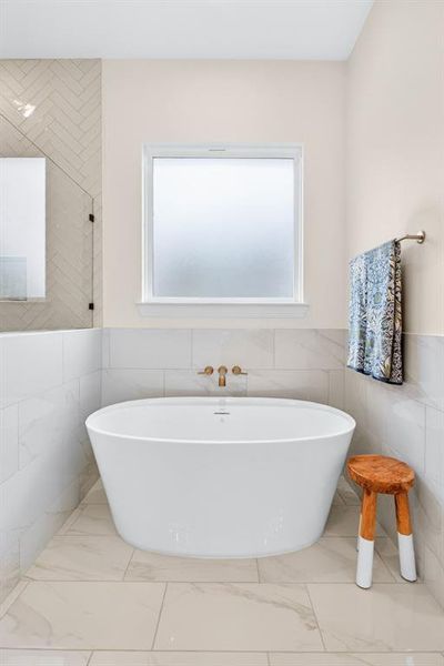 Full bath with tile walls, wainscoting, a freestanding tub, and light marble finish floors Full bath with tile walls, wainscoting, a freestanding tub, and light marble finish floors