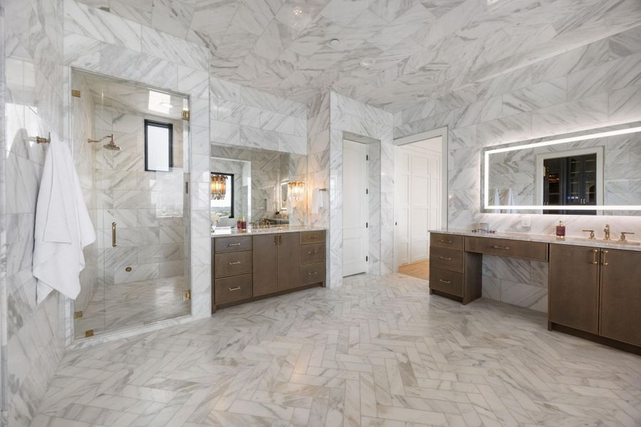 Marble-clad primary bathroom boasts a spacious shower and dual vanities with illuminated mirrors. Marble-clad primary bathroom boasts a spacious shower and dual vanities with illuminated mirrors.
