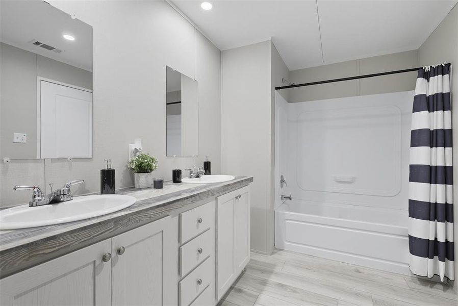Bathroom featuring shower / bath combination with curtain, double vanity, light wood-type flooring, and recessed lighting Bathroom featuring shower / bath combination with curtain, double vanity, light wood-type flooring, and recessed lighting