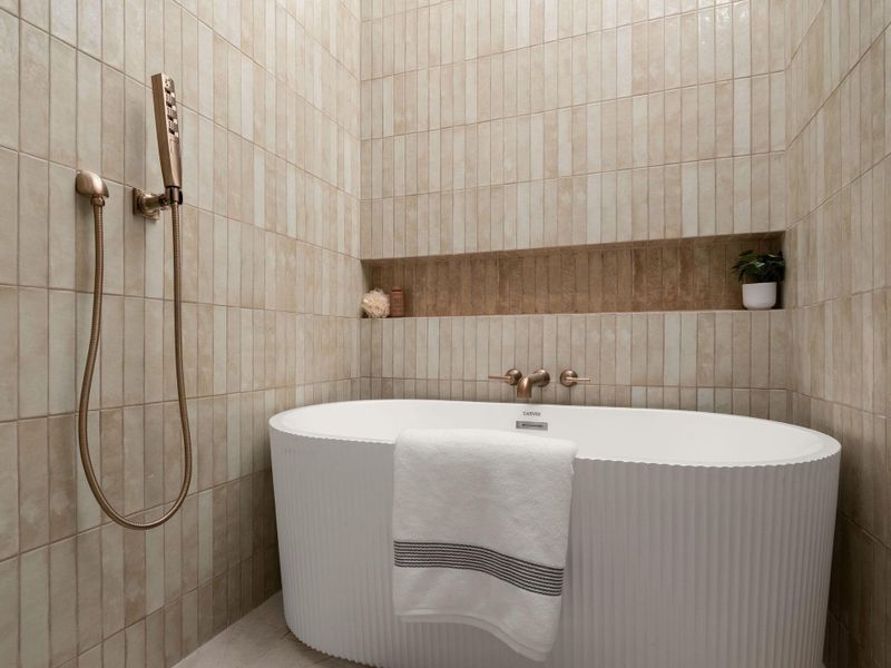 An elegant soaking tub stands enveloped by vertical tiled walls and refined brass fixtures.