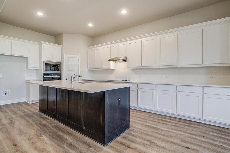 Kitchen with appliances with stainless steel finishes, light wood-type flooring, a kitchen island with sink, sink, and white cabinets