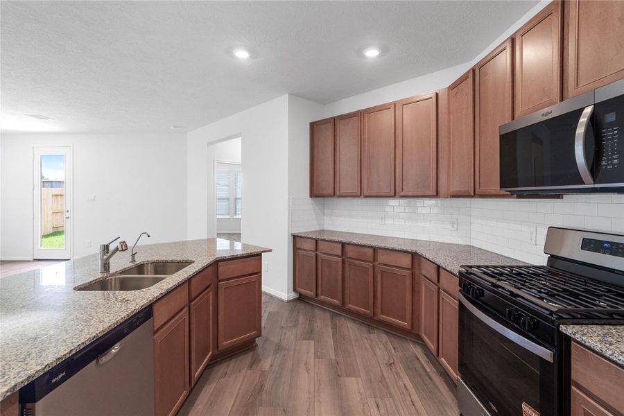 A true chef’s dream, this expansive kitchen boasts high ceilings, rich stained Woodmont Cody cabinets in Toffee stain, granite countertops in Iberian White, stainless steel appliances, a modern tile backsplash, recessed lighting, an island with a double sink, and a walk-in pantry—all with a clear view of the spacious Great Room. A true chef’s dream, this expansive kitchen boasts high ceilings, rich stained Woodmont Cody cabinets in Toffee stain, granite countertops in Iberian White, stainless steel appliances, a modern tile backsplash, recessed lighting, an island with a double sink, and a walk-in pantry—all with a clear view of the spacious Great Room.