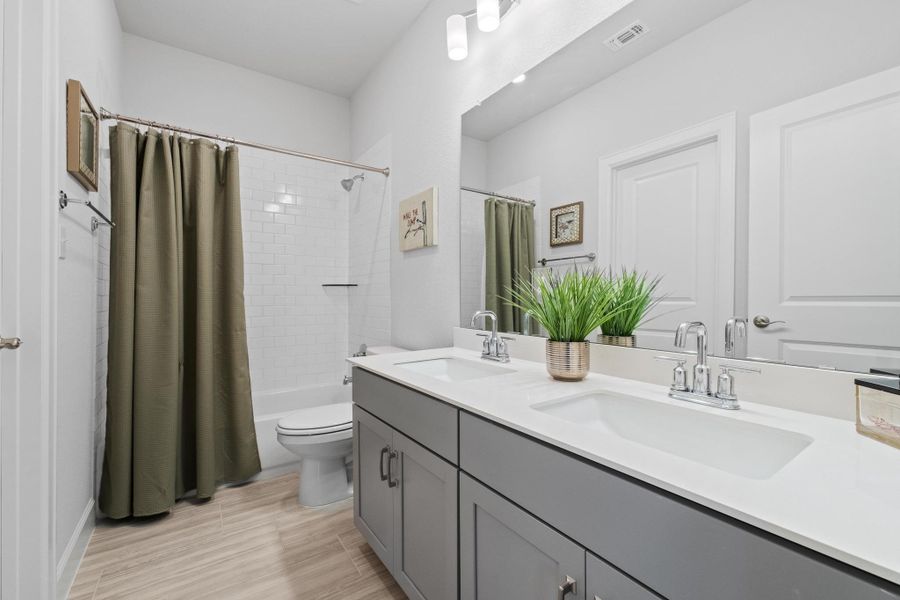 Full bathroom with double vanity, toilet, visible vents, and a sink Full bathroom with double vanity, toilet, visible vents, and a sink