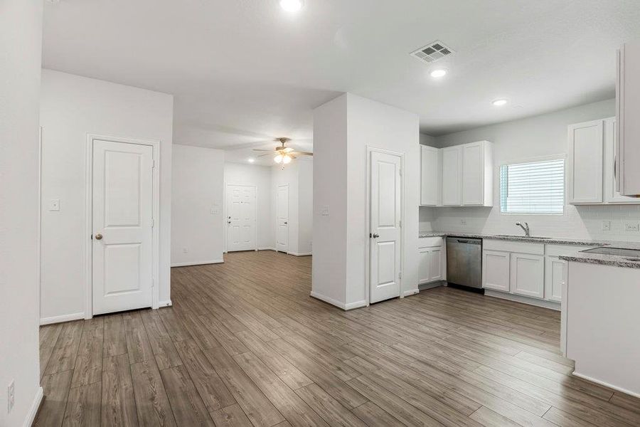 Kitchen featuring white cabinets, dishwasher, dark wood-type flooring, a ceiling fan, and light stone countertops