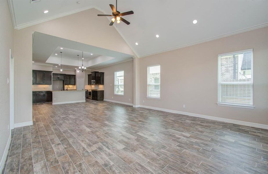 This is a spacious, open-concept living area with tile flooring, featuring a modern kitchen with dark cabinetry and a central island. The room is well-lit with natural light from multiple windows and enhanced by recessed lighting and a ceiling fan.