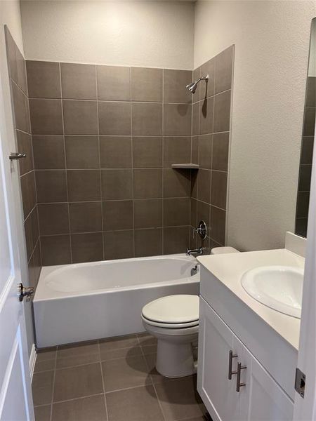 Full bath with shower / tub combination, vanity, a textured wall, and dark tile patterned floors