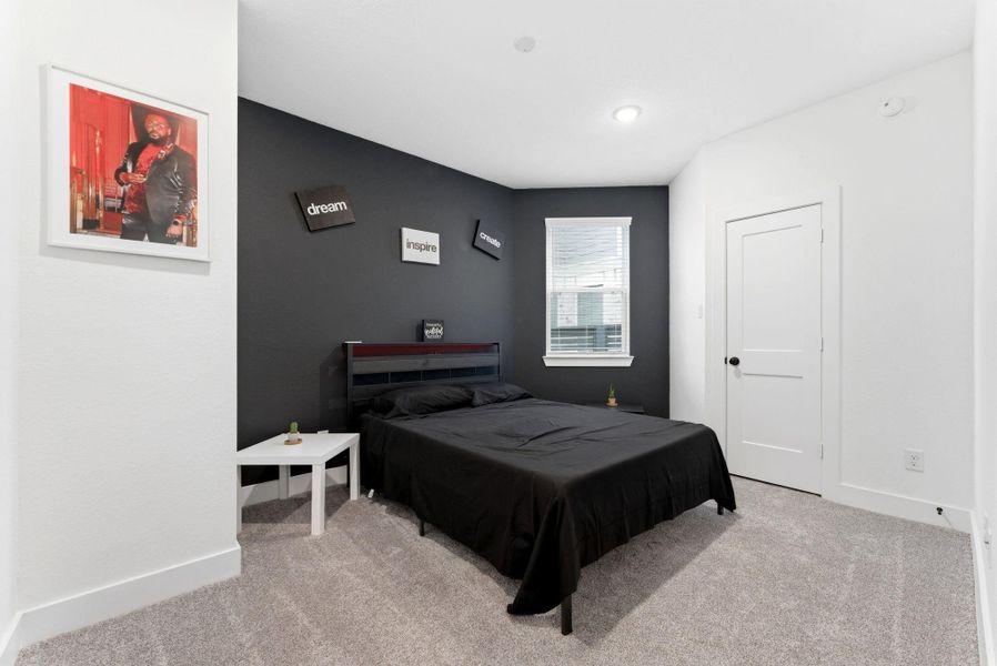 Comfortable secondary bedroom featuring plush carpet, a stylish accent wall, and natural light from the window.
