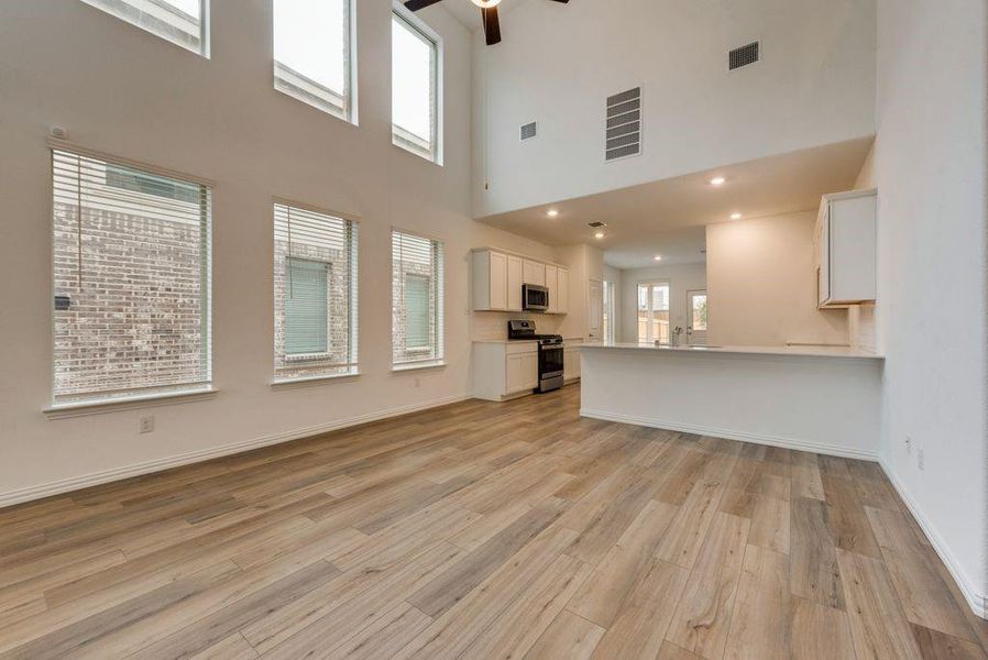 Unfurnished living room featuring sink, ceiling fan, light hardwood / wood-style floors, and a towering ceiling