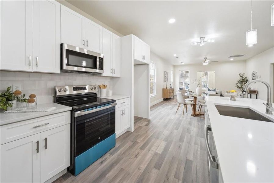 Kitchen featuring white cabinetry, light hardwood / wood-style flooring, stainless steel appliances, and decorative light fixtures