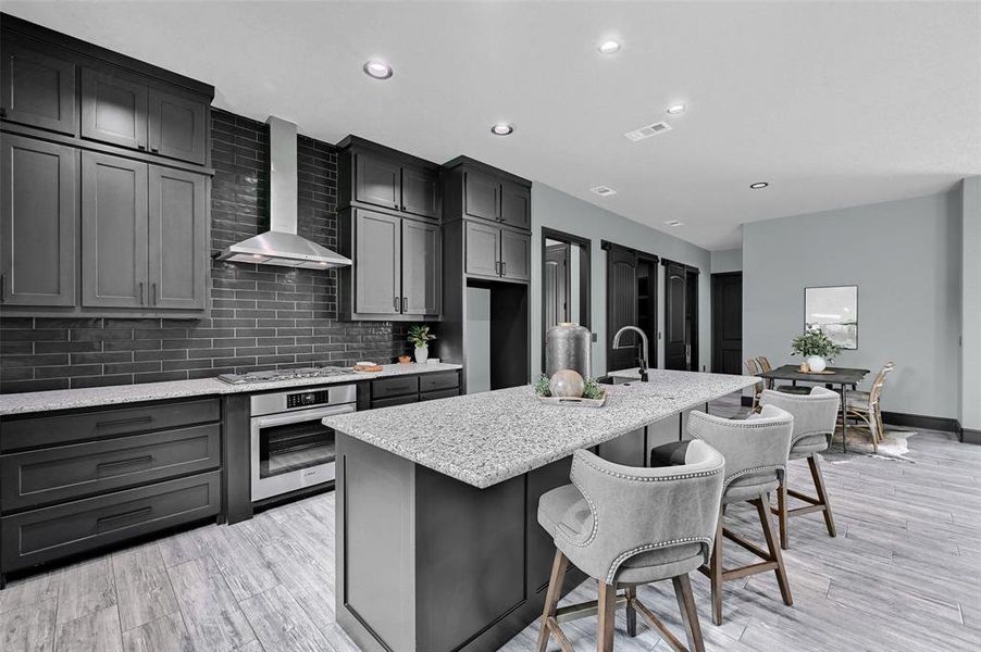 Kitchen with stainless steel appliances, wall chimney range hood, a kitchen island with sink, decorative backsplash, and light stone counters Kitchen with stainless steel appliances, wall chimney range hood, a kitchen island with sink, decorative backsplash, and light stone counters
