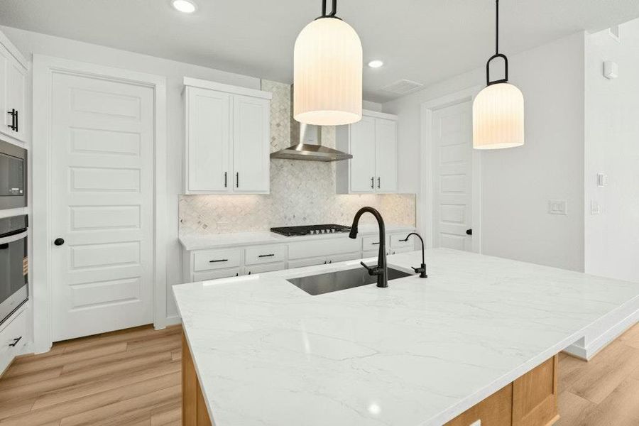 Kitchen with white cabinets, light stone counters, tasteful backsplash, decorative light fixtures, and an island with sink