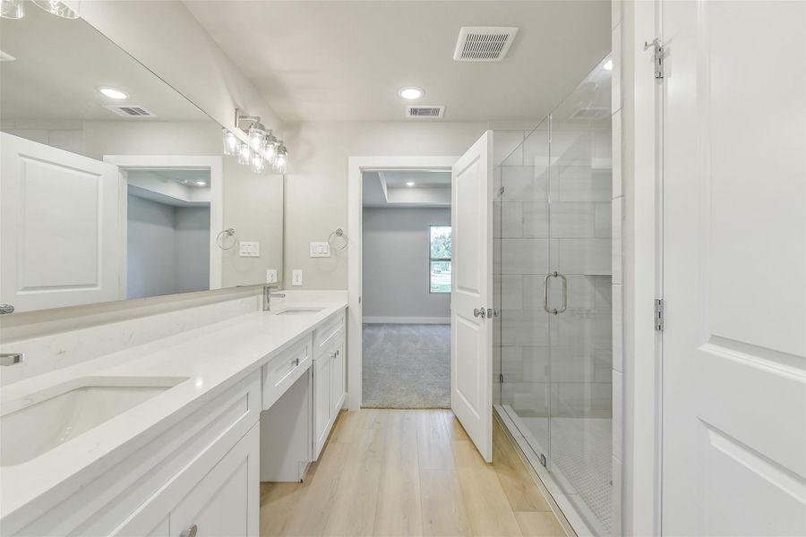 Elegant primary bath featuring dual vanities, a large mirror and walk-in shower with modern finishes throughout.