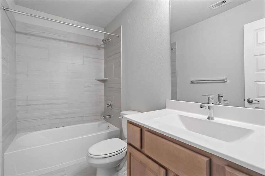 Secondary bath features tile flooring, bath/shower combo with tile surround, wood stained cabinets, beautiful light countertops, mirror, dark, sleek fixtures and modern finishes!