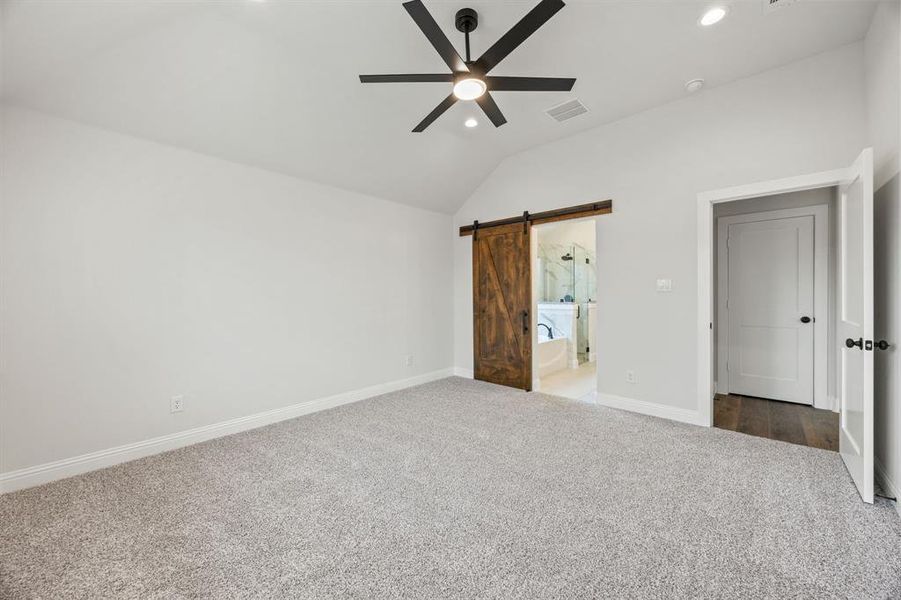 Unfurnished bedroom with carpet flooring, a barn door, a ceiling fan, vaulted ceiling, and recessed lighting