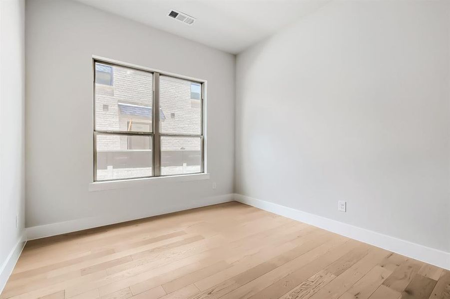 Light-filled room featuring a large window, light-toned wood-finish flooring, white baseboards, and neutral wall tones