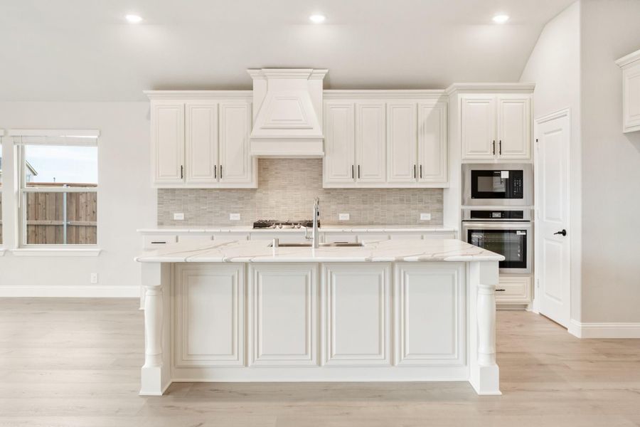 White kitchen with large center island, marble countertops, custom range hood, and stainless steel built-in appliances