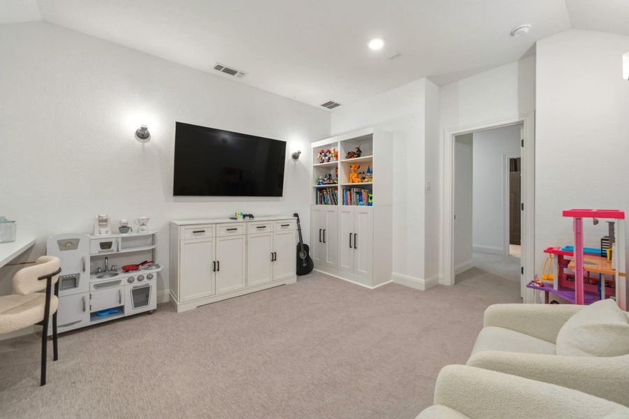 Spacious bonus room featuring sloped ceilings, recessed lighting, wall sconces, built-in desk areas, and a large built-in storage cabinets