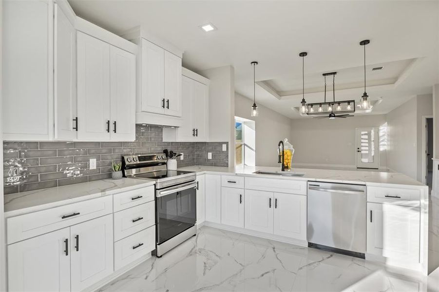 Kitchen with a tray ceiling, stainless steel appliances, decorative light fixtures, light marble finish flooring, and white cabinets