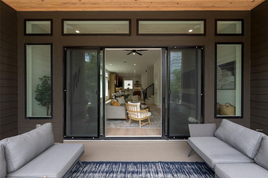 Warm cedar overhead, deep bronze cladding wrapping the opening, the living room framed like a picture just beyond the slider. Outdoor space that was clearly not an afterthought.