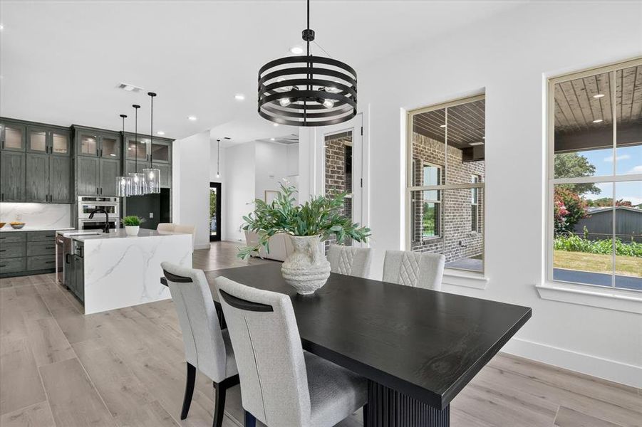 Open-concept dining area with wood-finish flooring, a modern black chandelier, and expansive windows