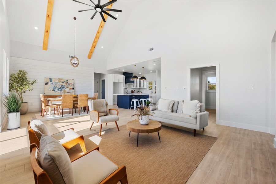 Living area with light wood finished floors, high vaulted ceiling, beam ceiling, wood walls, and recessed lighting