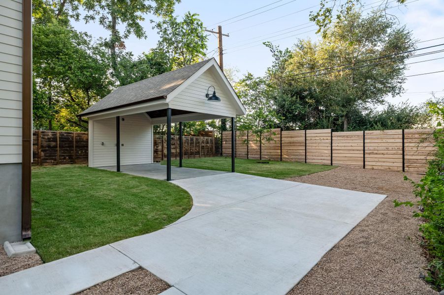 A newly installed concrete driveway curves gracefully toward a detached carport, offering ample off-street parking.