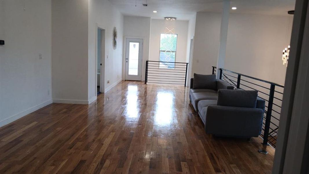 Expansive hardwood flooring throughout this open-concept space featuring a modern horizontal railing system, high ceilings, and recessed lighting