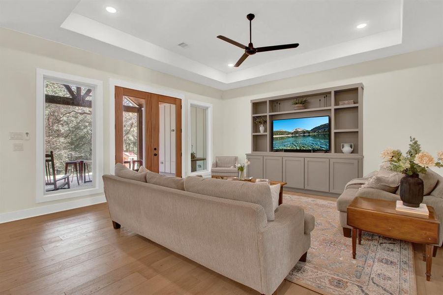 This is a bright, inviting living space featuring hardwood floors, recessed lighting, and large windows with a view of the outdoors. French doors lead to the back covered patio, enhancing the indoor-outdoor flow. The room includes a built-in entertainment center.