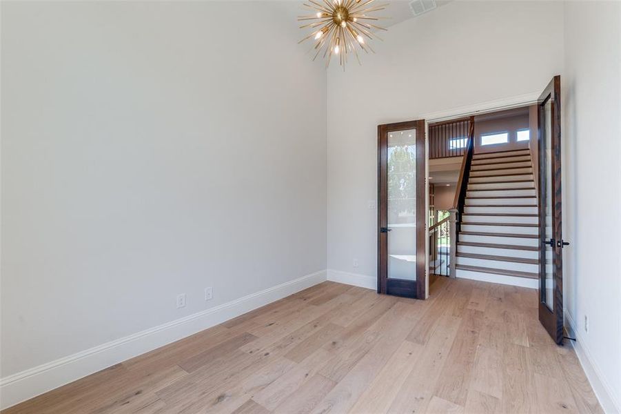 Spare room with stairs, light wood-style flooring, and a chandelier Spare room with stairs, light wood-style flooring, and a chandelier